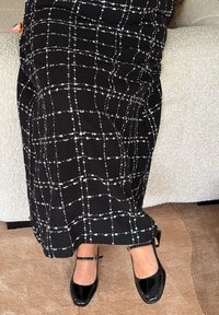 Crna suknja s bijelim uzorkom rešetke i teksturiranim materijalom, uparena s sjajnim crnim cipelama s remenčićima oko gležnja i kvadratnim vrhovima.