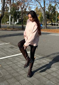 Oversized, soft pink jumper with long sleeves, teamed with black leggings and dark brown knee-high boots that have a chunky sole.