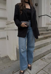 Juodas oversize švarkas, be petnešų juoda palaidinė, šviesiai mėlyni plačiakulkšniai džinsai ir juodi aštrūs tinkliniai aukštakulniai. Laiko dekoruoto juodo portfelio.
