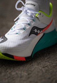 Bežecká obuv Saucony s bielym sieťkovaným zvrškom, čiernymi a červenými akcentmi, tyrkysovou podrážkou a jasne zeleným detailom na päte.