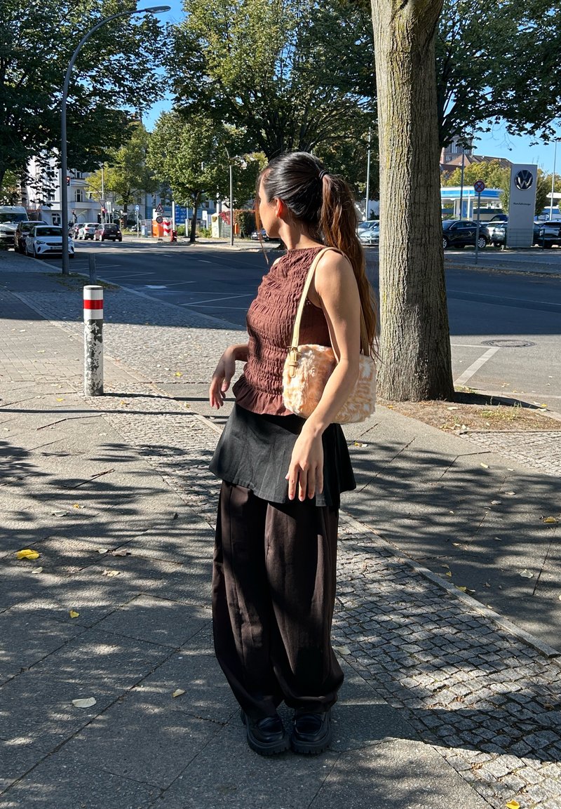Top castanho texturizado com design franzido, saia preta em camadas e calças pretas largas. Acessório: bolsa felpuda de cor pêssego.
