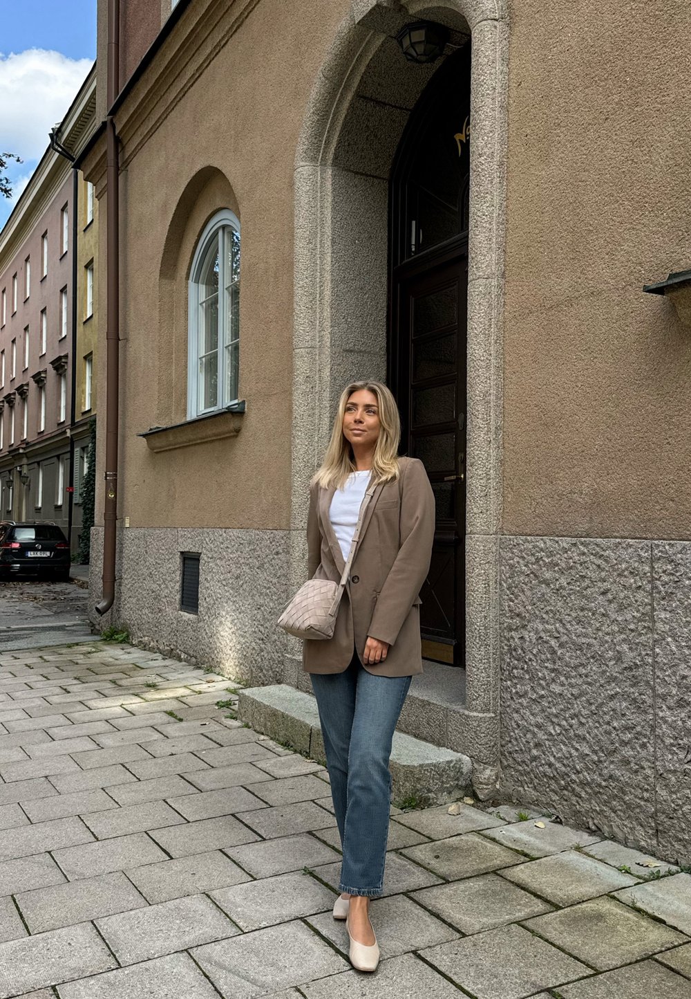 Bež oversize sakoi, bela srajca, svetlo modri kavbojke in bež čevlji na blok peto. Nositev tkanega svetlo bež torbice preko rame.