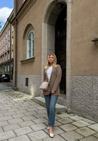 Bež oversize sakoi, bela srajca, svetlo modri kavbojke in bež čevlji na blok peto. Nositev tkanega svetlo bež torbice preko rame.