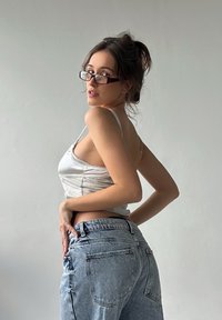 Een lichtgewicht, zilveren tanktop met dunne spaghettibandjes, gecombineerd met high-waisted, lichtblauwe denim jeans met achterzakken.