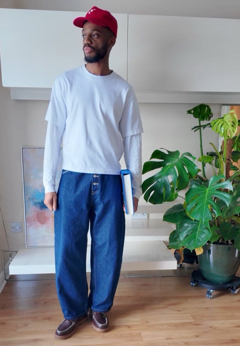 Witte lange mouwen shirt onder een cropped wit T-shirt, gecombineerd met losse spijkerbroek en bruine schoenen, met een blauw boek in de hand.