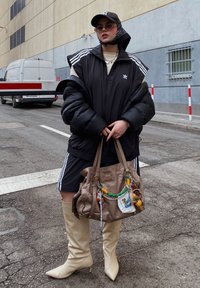 Isik, kes kannab musta Adidas spordiriietust, beeže kuni põlvedeni ulatuvaid saapaid, musta soojendajat, mütsi ja prille, hoiab suurlinna tänaval suurt pruuni käekotti.