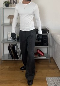 Fehér, hosszúujjú ing, fekete csíkos nadrág és fekete cipő. Kiegészítők között rétegelt nyakláncok és fekete kesztyűk találhatók. Fa padló háttér.