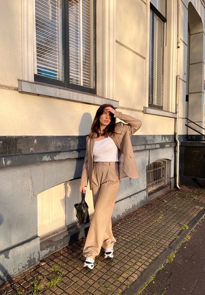 Traje beige de dos piezas con pantalones de pierna ancha y una chaqueta entallada, combinado con una camiseta sin mangas blanca y un bolso negro. Zapatillas deportivas casuales.