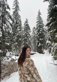 Fleecejacke mit einem braunen, beige und grünen abstrakten Muster, hohem Kragen und lässiger Passform, getragen in einem schneebedeckten Wald.