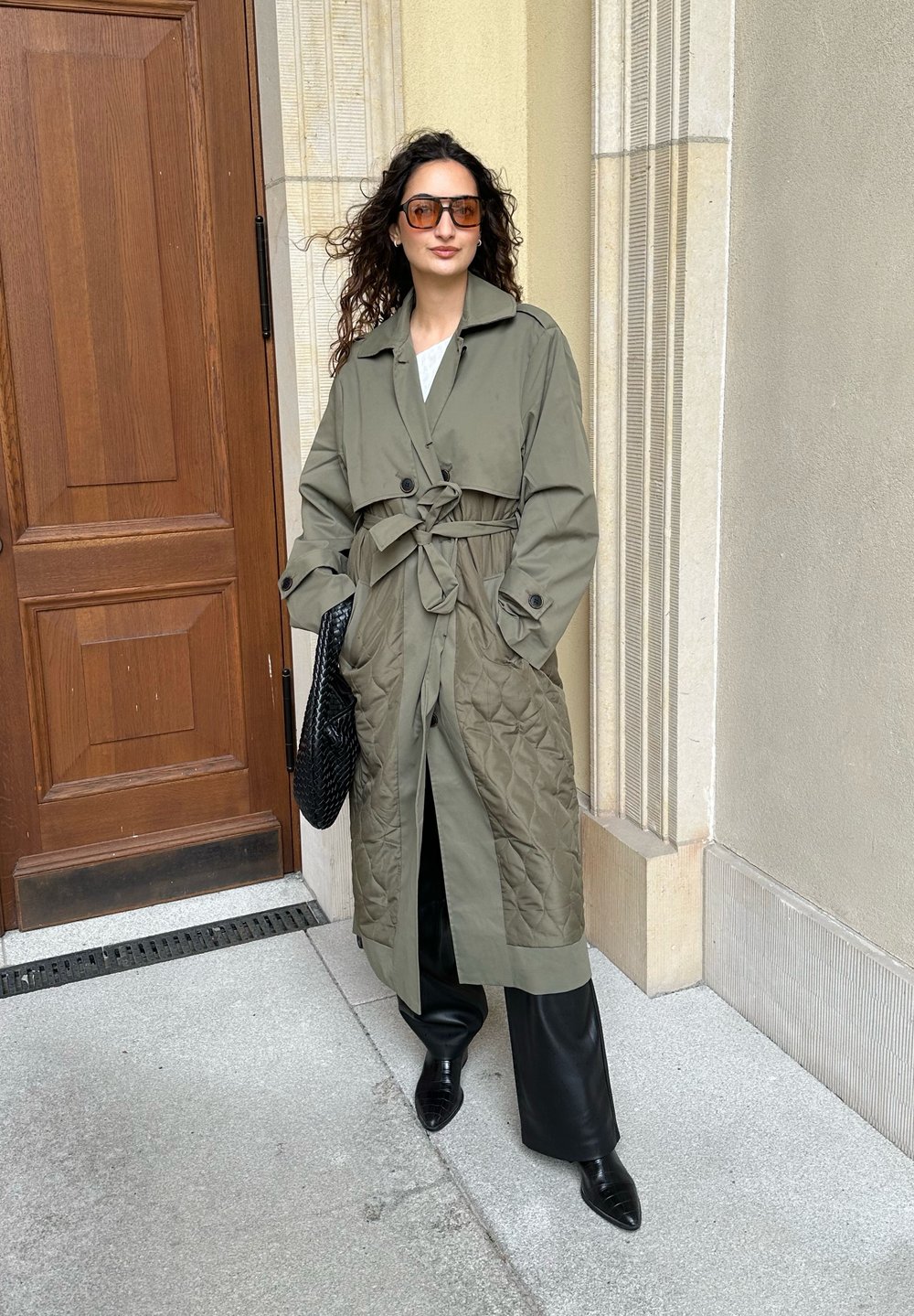 Ελαιόχρωμο παλτό με επενδεδυμένο κάτω μέρος, μπροστινή ζώνη και μεγάλες τσέπες, σε συνδυασμό με μαύρο δερμάτινο παντελόνι και μυτερές γόβες.