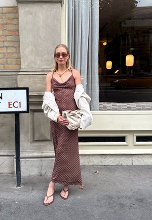 Vestido marrón de lunares con un corsé ajustado y tirantes finos, combinado con una chaqueta blanca de gran tamaño, sosteniendo un bolso beige.