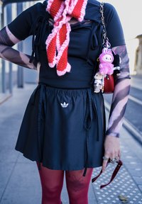 Svart atletisk miniskjørt med elastisk midjebånd og knyting, med Adidas-logo. Lagdelt svart topp og strikket skjerf i rosa og rødt.