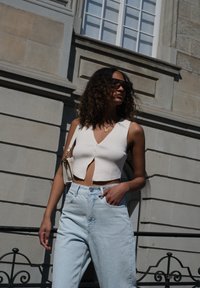 White ribbed crop top with a V-neck and front buttons, teamed with light blue high-waisted jeans. Accessories include a small white bag.
