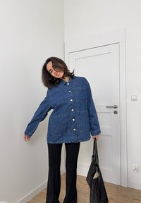 Džínová bunda tmavě modré barvy s knoflíkovým zapínáním, dvěma velkými kapsami a klopov�ým límcem, v kombinaci s černými rozšířenými kalhotami a černou kabelkou.