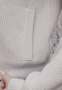 Lysegrå strikkegenser med ribbestruktur og detalj med sidelomme. Lange ermer med tettsittende mansjett og en avslappet passform.