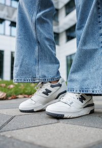 Λευκά αθλητικά παπούτσια με γκρι λεπτομέρειες, με υφασμάτινο δέρμα, κλείσιμο με κορδόνια και καουτσούκ σόλα, συνδυασμένα με ανοιχτό μπλε τζιν παντελόνι.
