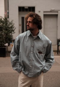 Ριγέ πουκάμισο σε μπλε και λευκό με τσέπη; άνετη εφαρμογή, μακρυά μανίκια και κλασικό γιακά. Φοριέται με ανοιχτόχρωμο παντελόνι.