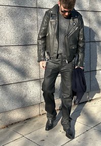 Fekete bőr motoros dzseki szürke pulóverrel, fekete bőr nadrággal és hegyes orrú fekete csizmákkal párosítva. Egy tengerészkék sálat tartanak.