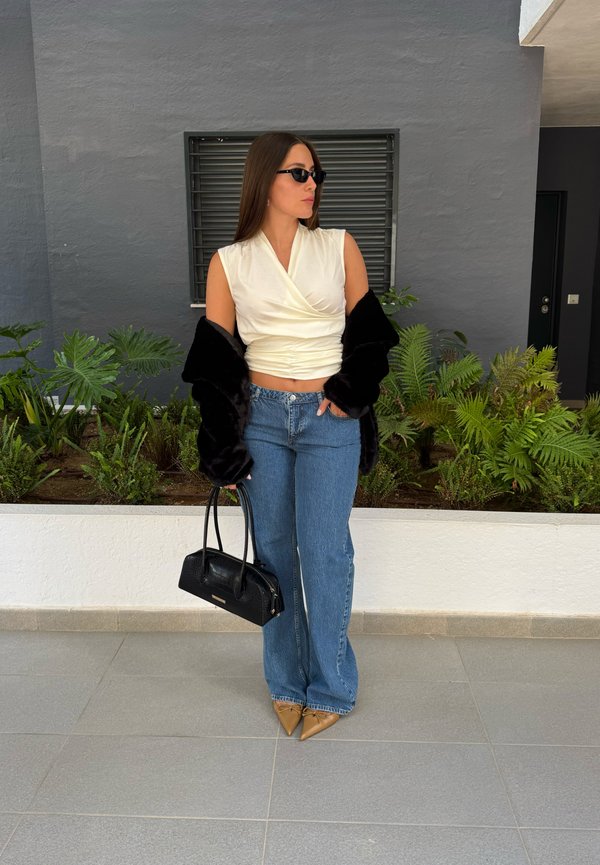 Off-white, zavito stil zgornji del s teksturirano površino, v kombinaciji z svetlo modrimi, razširjenimi kavbojkami. Črn umetni krzneni šal in ožji nude petki dopolnjujejo videz.