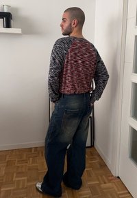 Hosszú ujjú ing textúrált kék és piros mintával, laza farmernadrággal párosítva, amelyen látható varrások és hátsó zseb található.