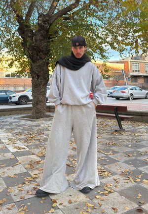 Sudadera gris de gran tamaño y pantalones deportivos anchos a juego, hechos de tela suave, combinados con una bufanda negra y zapatos oscuros.