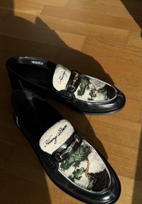 Mocassins en cuir noir avec inserts en tissu crème texturé arborant un motif camouflage vert et marron ainsi qu'un détail de mors doré.