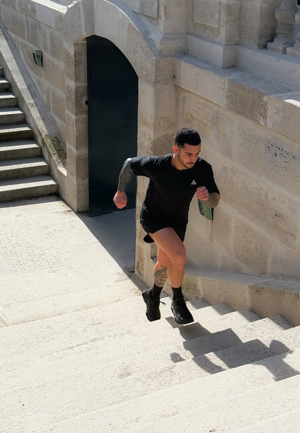 Férfi fekete sportfelszerelésben szabadtéri kőlépcsőn fut fel egy íves bejáratú történelmi épület mellett.