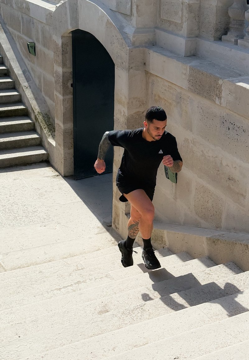 Man in black athletic gear running up outdoor stone steps beside historic building with arched doorway.