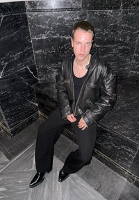 Musta nahkatakki vetoketjulla ja kahdella rintataskulla, yhdistetty tiukkaan mustaan toppiin ja leveisiin mustiin housuihin. Kiiltävät mustat kengät.