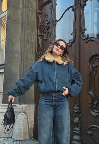 Denim-bomberjakk kunstkarusnahast kraega, kombineeritud kõrge vöökohaga laia säärega teksadega. Tumesinine värv, kantud koos mustade päikeseprillide ja käekotiga.