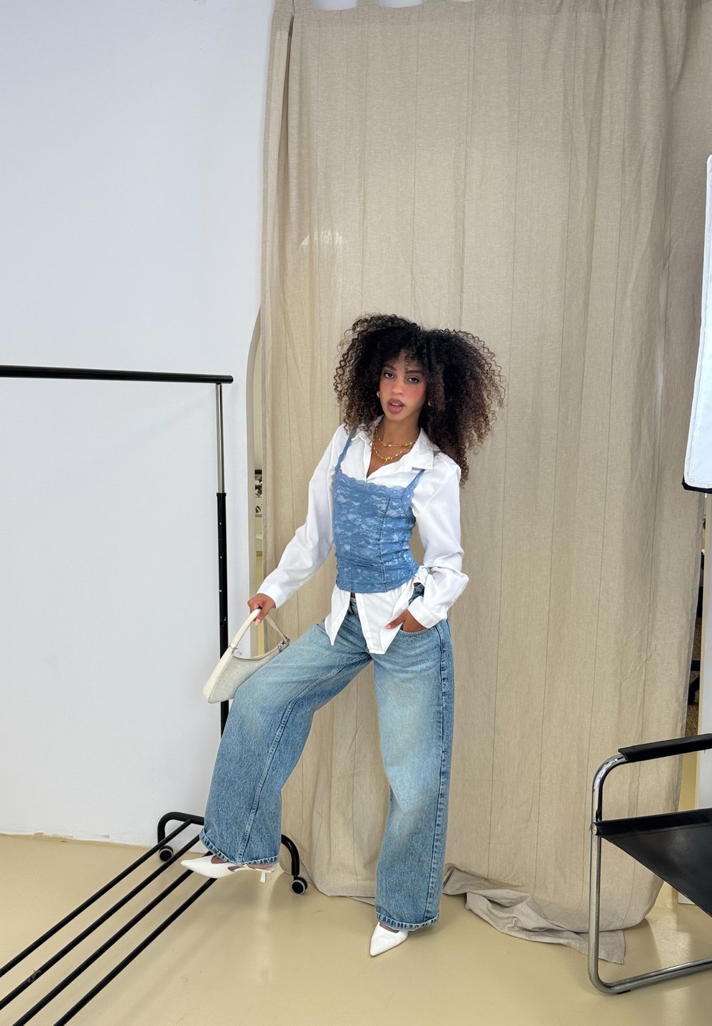 Blå spids corse over en hvid skjorte, parret med brede falmede jeans og hvide spidse hæle. Modellen holder en lille hvid håndtaske.
