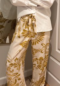 Pantalones color crema con un patrón floral mostaza, con cintura de cordón y pierna ancha, con una textura de tela suave y ligera.