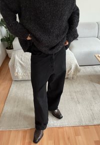 Pull noir surdimensionné avec un motif en maille texturée, associé à un pantalon noir ample et des chaussures foncées à bout pointu.