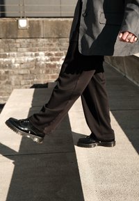 Melni bikses ar brīvu piegriezumu, apvienotas ar spīdīgām melnām lace-up kurpēm ar biezu, caurspīdīgu zoli un dekoratīvām aparatūras akcentiem.