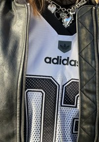 Adidasova majica z mešano teksturo v črni in beli barvi, z velikimi črnimi številkami. Prekrita z usnjenim črnim zip jopičem z prešito površino.