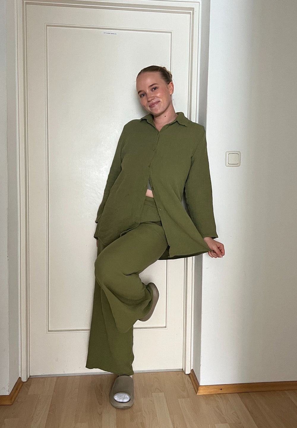 Conjunto de duas peças verde-oliva composto por uma camisa de botão de mangas longas e calças de perna larga. Design simples, textura suave, com calçado cinza.