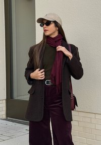 Ruskea kalanruotokuvioinen pikkutakki, tummanvihreä paita, viininpunainen huivi, violettiväriset corduroyhousut, vaaleanbeige lippalakki ja mustat aurinkolasit. Hopeinen vyökoristelu näkyvissä.