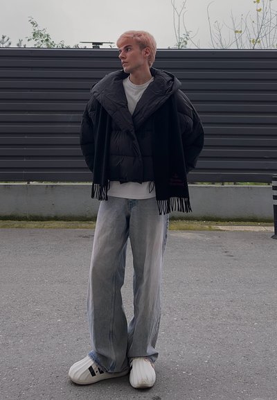 Chaqueta acolchada negra, sobre una camiseta blanca, combinada con jeans sueltos de mezclilla azul claro y calzado blanco de gran tamaño.