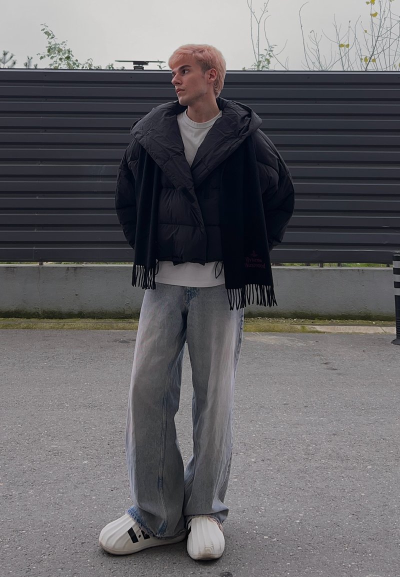 Doudoune noire portée sur un t-shirt blanc, associée à un jean en denim bleu clair ample et à des chaussures blanches surdimensionnées.