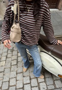 Maglietta a righe marroni e bianche con maniche lunghe, jeans a campana di colore azzurro chiaro, calzature beige e una piccola borsa beige con tracolla intrecciata.