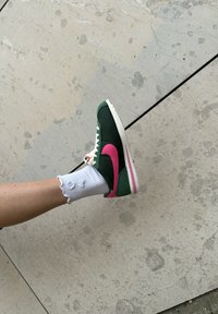 Grønne og rosa Nike-sko med en hvit såle, med en teksturert overdel og distinkt swoosh-logo, sammen med en hvit ribbestrikket sokk.