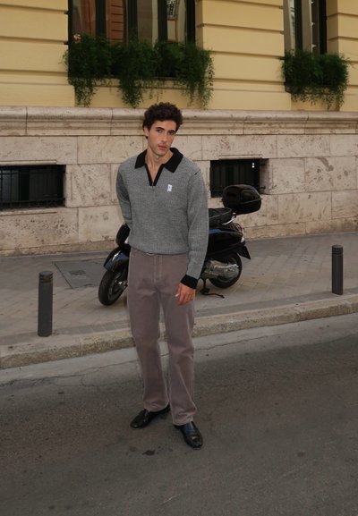 Suéter a cuadros en gris y negro con cuello, combinado con pantalones de pana color marrón claro y zapatos negros, de pie en una calle.