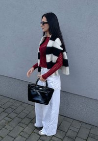 Μαυρόασπρη ριγωτή κάπα, μπορντό δαντελένιο τοπ, λευκά παντελόνια με φαρδύ πόδι, κρατώντας μια μαύρη τσάντα χειρός με φερμουάρ. Τα υποδήματα είναι ανοιχτού γκρι.