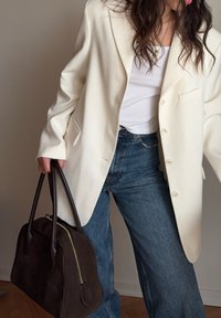Hvit oversized blazer, teksturert stoff, enkelt knappelukking, kombinert med en tettsittende hvit topp og høyt midje denim. Brun strukturert håndveske.