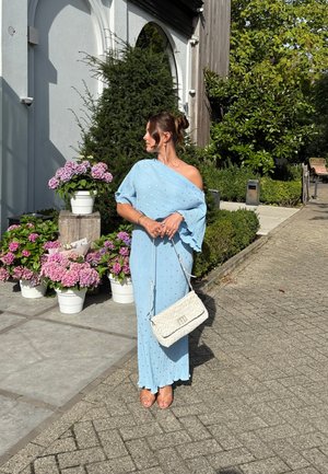 Vestido azul claro con diseño de hombros al aire, tejido texturizado y adornos de cuentas. Bolso blanco con correa de cadena. Fondo floral.