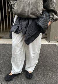 Černé prošívané psaníčko, šedá mikina s kapucí, černobílá kostkovaná košile svázaná v pase, bílé volné kalhoty, černé boty s rozdělenými špičkami.