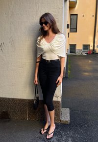 Bijela bodysuit s drapiranim nikom na ramenima, crne hlače visokom struku, crne japanke i mala crna torbica.