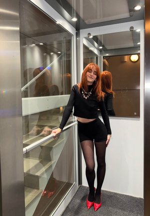 Top corto negro de canalé y pantalones cortos, medias negras estampadas, tacones rojos. Ascensor reflectante con detalles de vidrio y metal.