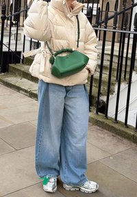 Veste matelassée beige avec une ceinture nouée, jean large bleu, et sac à main vert avec une sangle nouée. Les baskets ont un motif en mesh et des détails réfléchissants.