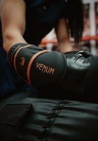 Inimene, kes kannab musta Venumi poksikindaid, lööb jõusaalis musta nahast poksikotiga.